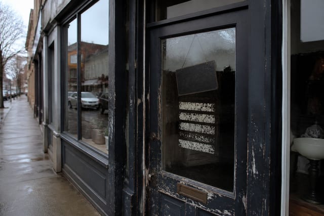 A closed UK shop door with worn opening-hours stickers on rain-spotted glass.